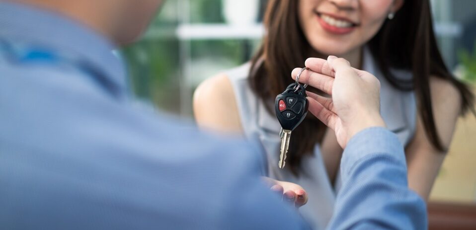 Woman receiving remote car key from dealer young sales man for buy new car, or vehicle rental in automobile showroom office, customer service satisfaction and auto business concept